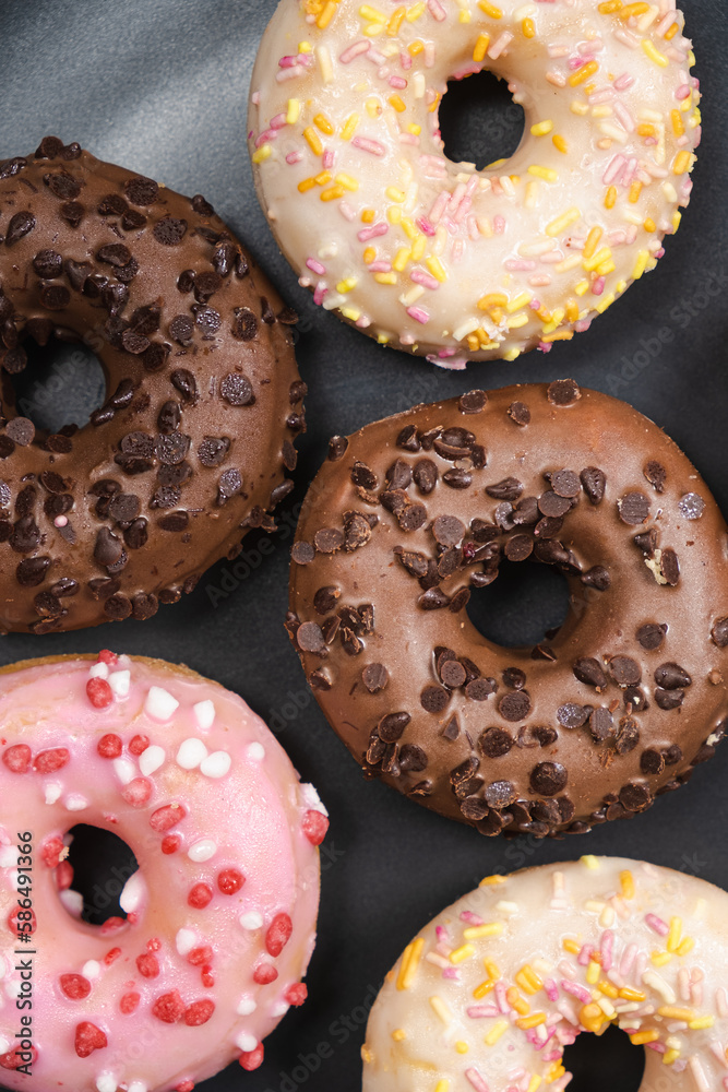 Lots of little donuts with white, pink and chocolate glaze on a black plate, top view Lots of little donuts with white, pink and chocolate glaze on a black plate, top view