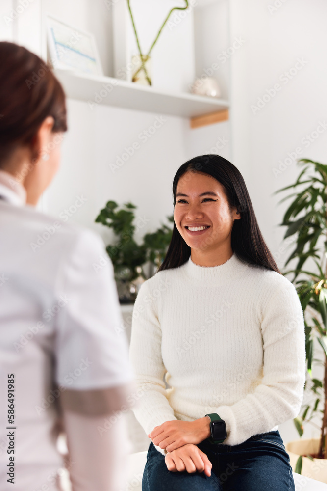 A happy Asian female patient talking with a female dermatologist at the clinic. A happy Asian female patient talking with a female dermatologist at the clinic.
