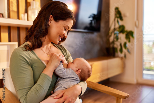 Happy mother holding her newborn child during breastfeeding at home.