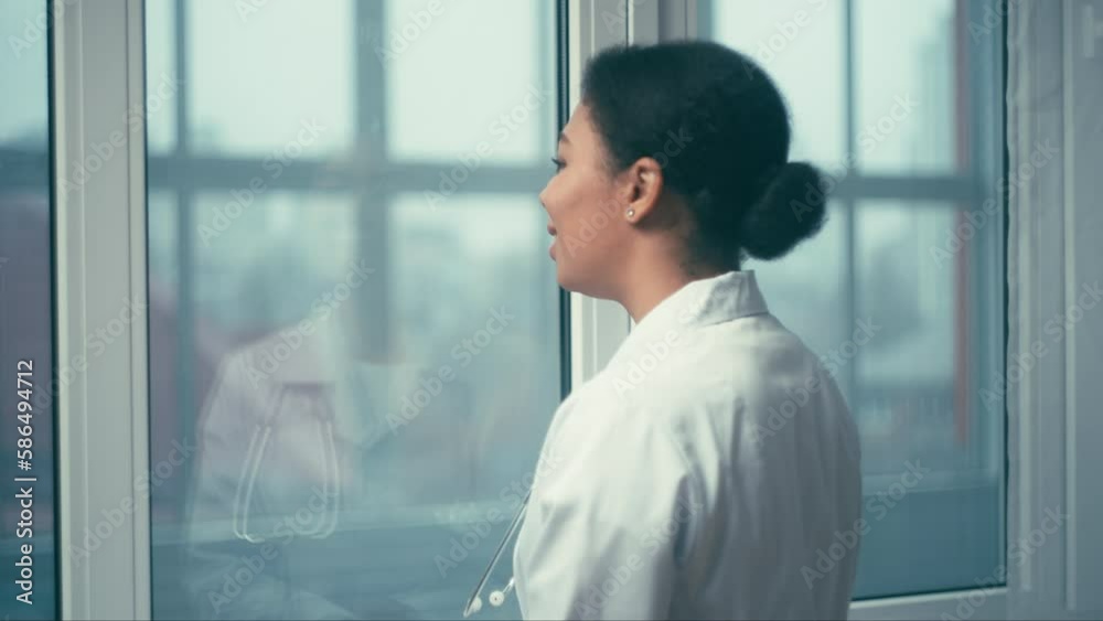 Pensive female therapist looking in window and smiling, happy with good news Pensive female therapist looking in window and smiling, happy with good news