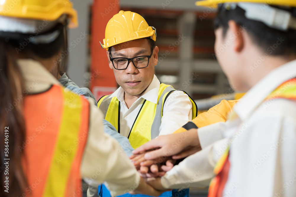 Group of male and female factory workers standing putting their hands together in industry factory. Factory workers stack of hands in factory. Unity and teamwork concept Group of male and female factory workers standing putting their hands together in industry factory. Factory workers stack of hands in factory. Unity and teamwork concept