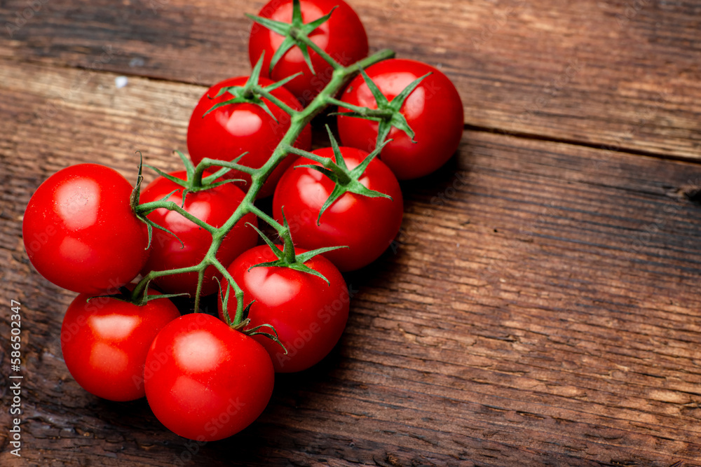 Branch of fresh cherry tomatoes on a brown wooden background. Branch of fresh cherry tomatoes on a brown wooden background.