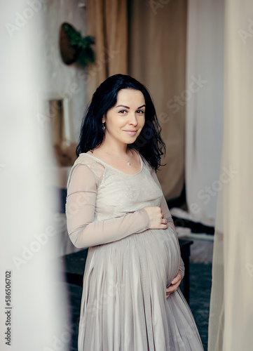 Young pregnant woman with long healthy hair, holds her belly and looking at it with love
