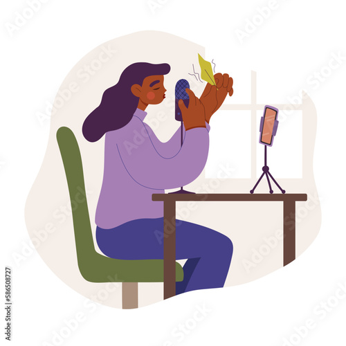 Girl or young woman sits at desk in front of smartphone and records the whispering and rustling of paper on microphone. Recording sounds and voices for ASMR content, podcast or blog.