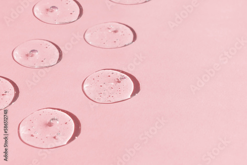 Drops of serum or hyaluronic acid gel with bubbles on a pink background. Smears of cosmetic skin care products. Wellness and beauty concept.