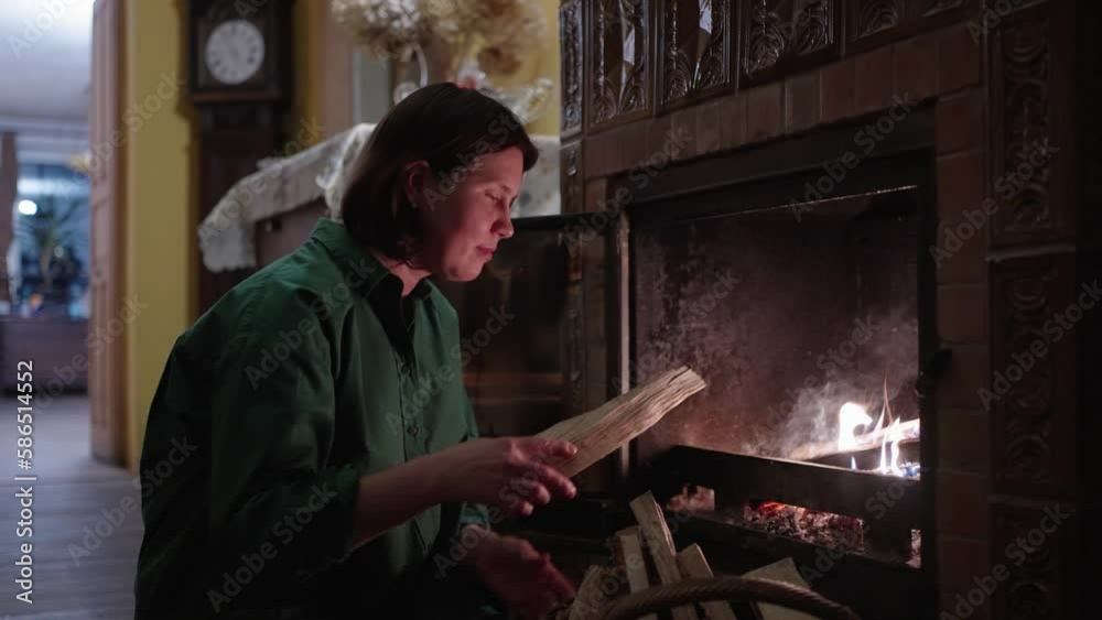 A woman putting firewood into a fireplace, keeps a fire burning A woman putting firewood into a fireplace, keeps a fire burning