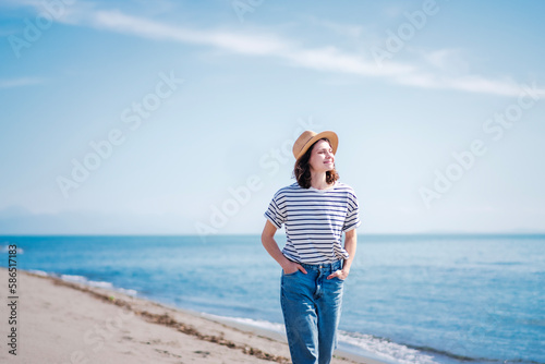 Young happy woman in a hat walking along the sandy beach on the blue sea. Summer holidays and travel concept photo