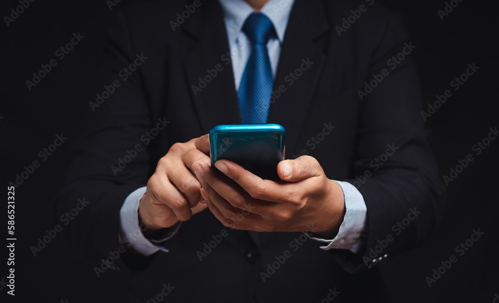 Businessman in a suit using a smartphone while standing on a black background Businessman in a suit using a smartphone while standing on a black background