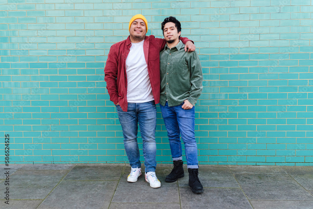Happy brothers standing together in front of turquoise brick wall Happy brothers standing together in front of turquoise brick wall