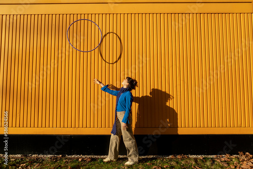 Young woman tossing hula hoop near yellow container on sunny day photo