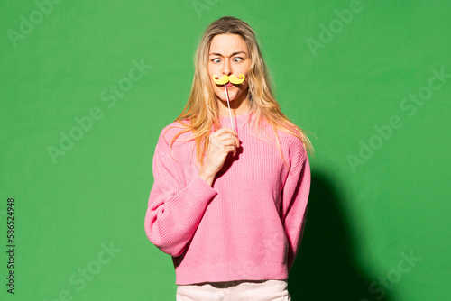 Blond woman imitating mustache standing against green background photo
