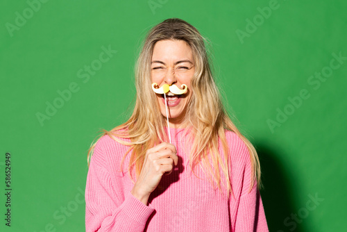 Happy woman imitating fake mustache against green background