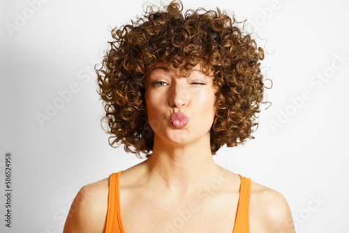 Woman with curly hair puckering face against white background photo