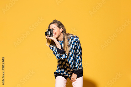 Happy woman photographing with camera against yellow background photo