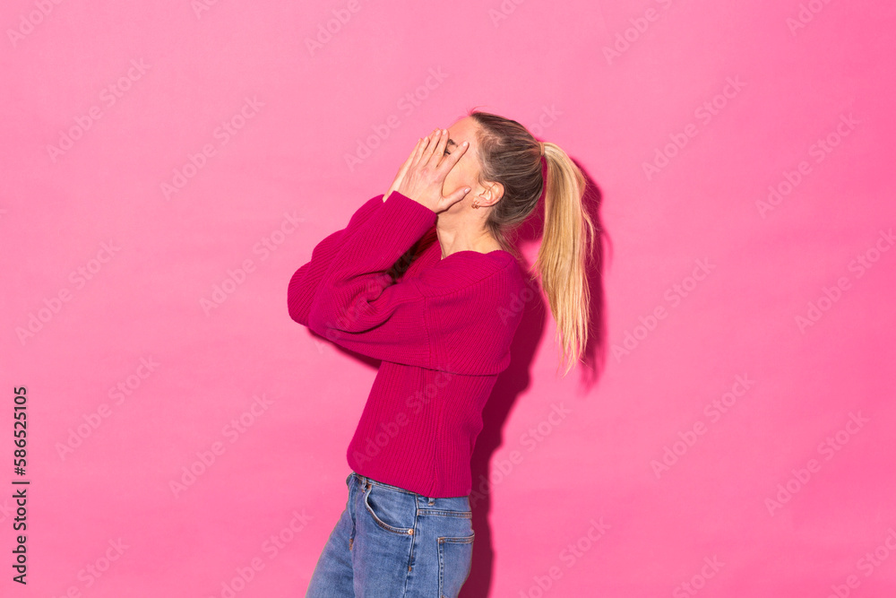 Woman covering face with hands standing against pink background Woman covering face with hands standing against pink background