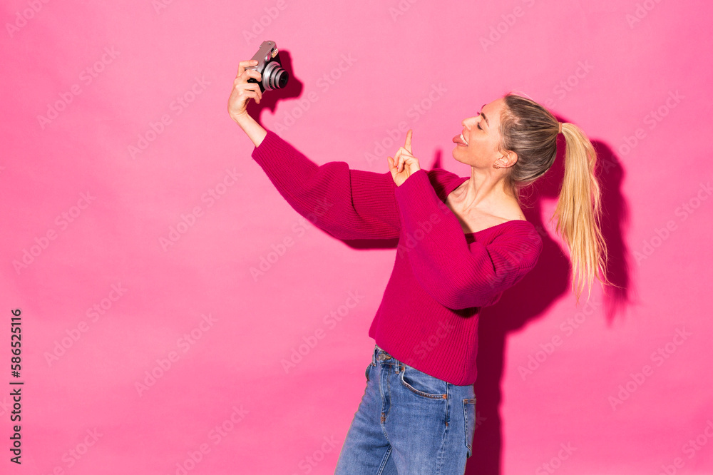 Woman gesturing peace and taking selfie from camera against pink background Woman gesturing peace and taking selfie from camera against pink background