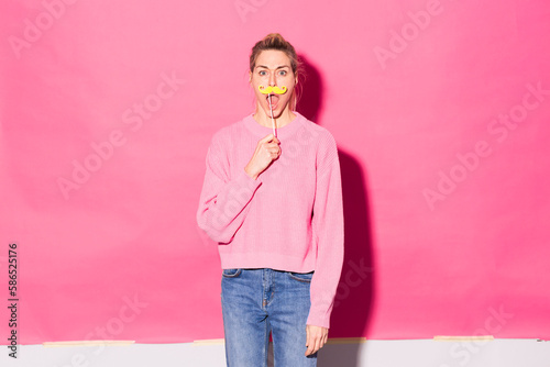 Woman holding fake mustache standing against pink background photo