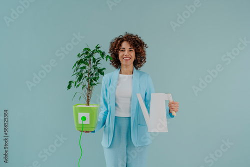 Happy woman holding electric plug inserted in potted plant and watering can photo