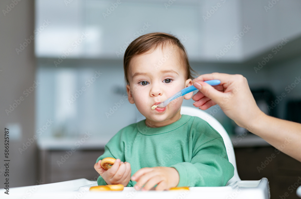Baby eating food on kitchen. Mother feeding son puree Baby eating food on kitchen. Mother feeding son puree