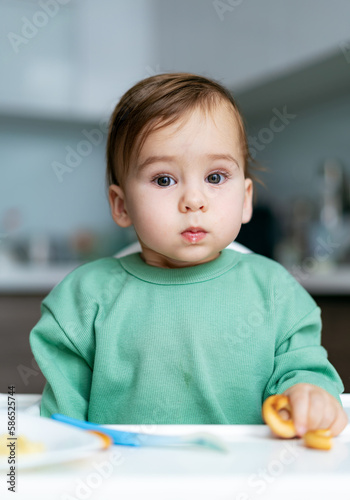 Baby eating food on kitchen. Adorable baby boy eating cookies sitting in highchair