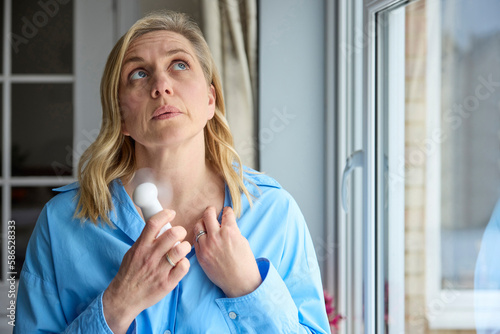 Menopausal Mature Woman Having Hot Flush At Home Cooling Herself With Handheld Electric Fan
