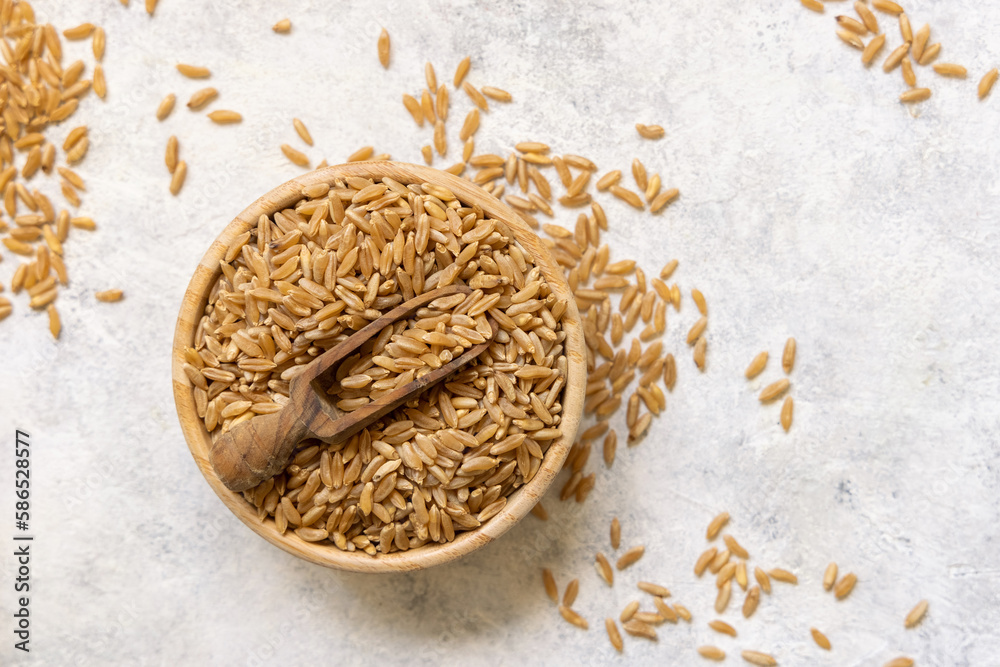 Bowl of raw dry rye grain with a wooden spoon on white table top view Bowl of raw dry rye grain with a wooden spoon on white table top view