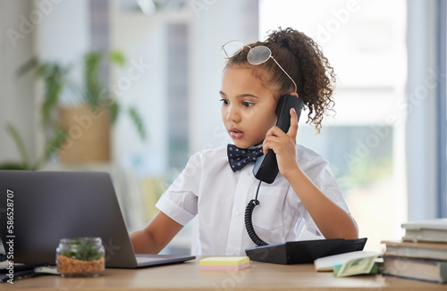 Children, telephone and a girl having fun in an office as a fantasy businesswoman at work on a laptop. Kids, phone call and a female child working at a desk while using her imagination to pretend photo