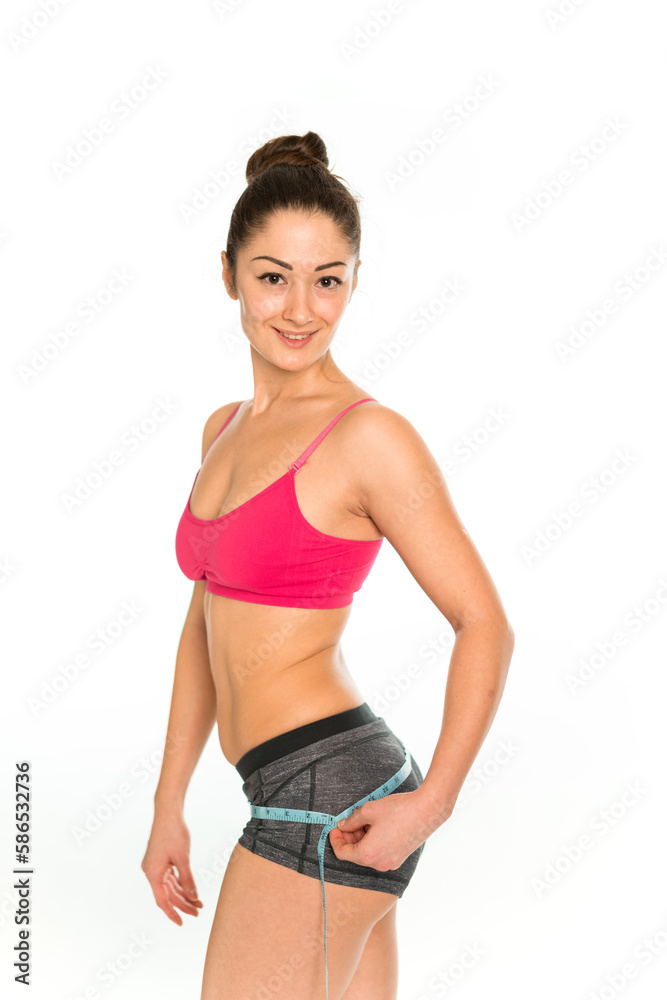 Pretty fit asian smiling woman in sport wear measure hips. Flat stomach with measuring tape. Measuring a woman's waist with a measuring tape. Concept of sport, healthy diet, fitness lifestyle. Pretty fit asian smiling woman in sport wear measure hips. Flat stomach with measuring tape. Measuring a woman's waist with a measuring tape. Concept of sport, healthy diet, fitness lifestyle.
