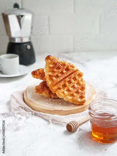 Selective focus of Croffel covered in honey or croissant waffle as breakfast or snack. White table background. Eye level angle photo