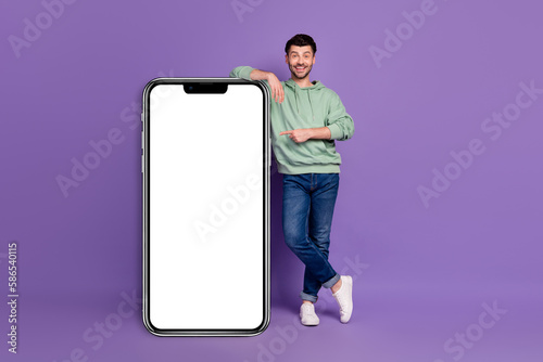 Full length photo of nice young man lean point vertical device screen wear trendy gray outfit isolated on violet color background © deagreez