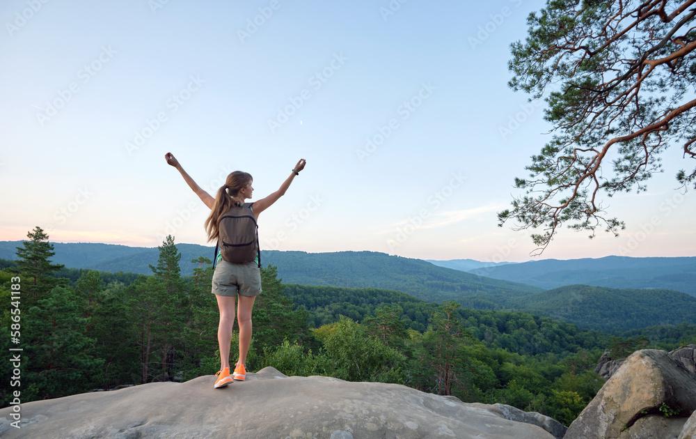Hiker woman standing on mountain footpath raising up hands enjoying evening nature during travel on wilderness trail. Lonely female traveler traversing high hilltop route. Healthy lifestyle concept Hiker woman standing on mountain footpath raising up hands enjoying evening nature during travel on wilderness trail. Lonely female traveler traversing high hilltop route. Healthy lifestyle concept