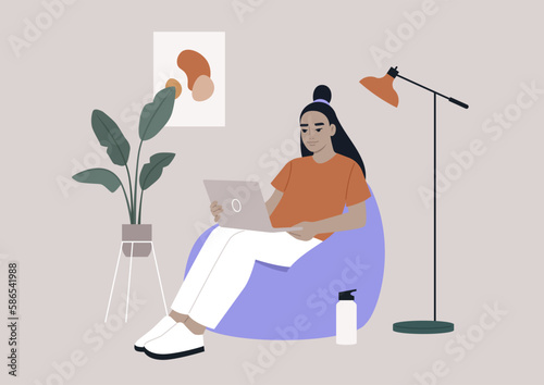 an Asian hipster character sits on a bean bag while typing on their laptop in their home office