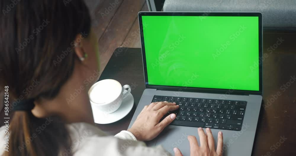 Over the shoulder shot business woman working at cafe interior on laptop computer looking at green screen. Freelancer person using laptop computer with laptop green screen sitting at coffee shop table