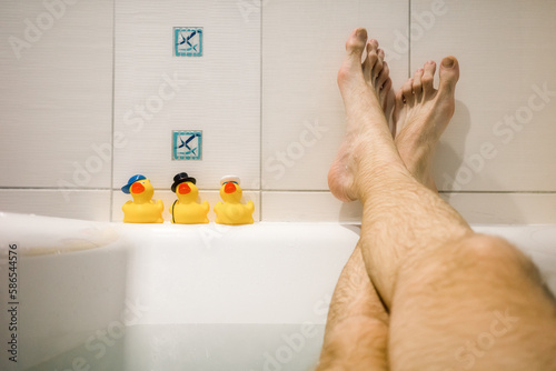Obraz na plátně Legs of man relaxing in the bath and yellow ducks