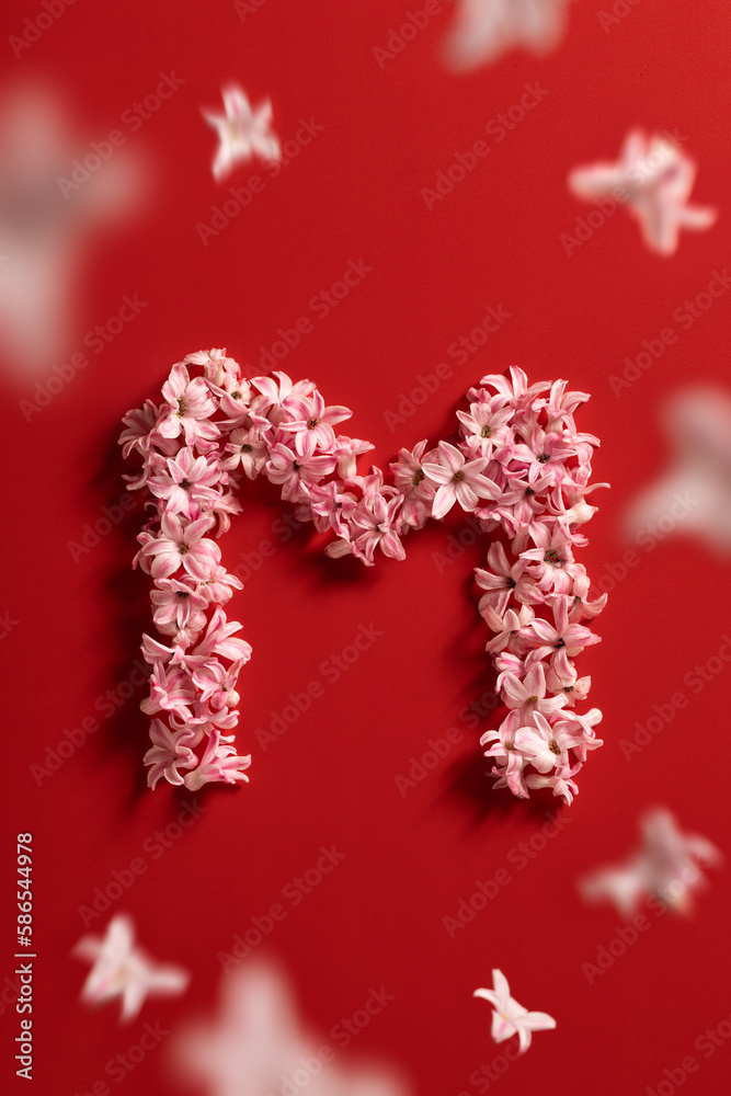 Letter M made from pink hyacinth and flying petals isolated on a red background. Flat lay, top view. Spring blossom concept for wedding, women, Mother, 8 March, Valentine's day