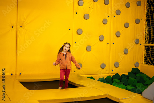 Little girl kid jumping on trampoline at yellow playground park. Child in motion during active entertaiments.