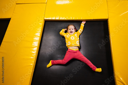 Baby girl kid lying on trampoline at playground park. Child in motion during active entertaiments. photo