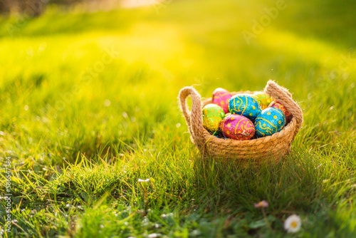 Easter eggs in basket in grass. Colorful decorated easter eggs in wicker basket. Traditional egg hunt for spring holidays. Morning magical light. photo