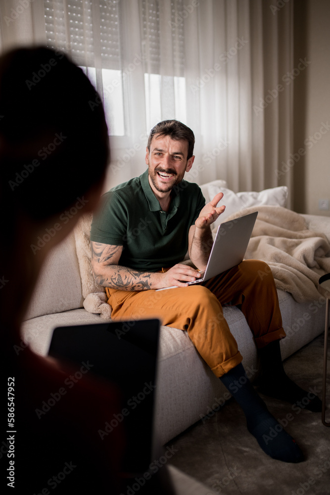 Fototapeta premium Happy young man with tattoos working from home, talking to his wife.