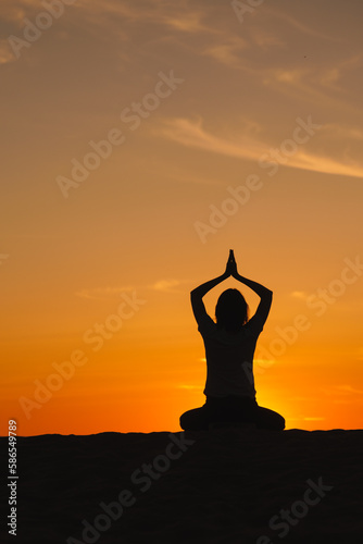 Fototapeta Naklejka Na Ścianę i Meble -  yoga meditation, silhouette of woman at sunset in lotus position. health recreation and sports, outdoor training. poster, postcard. person is engaged in breathing practices on seashore. mental health