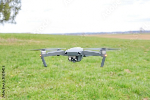 A flying quadrocopter against the background of grass in cloudy weather takes pictures of the surface of the earth.