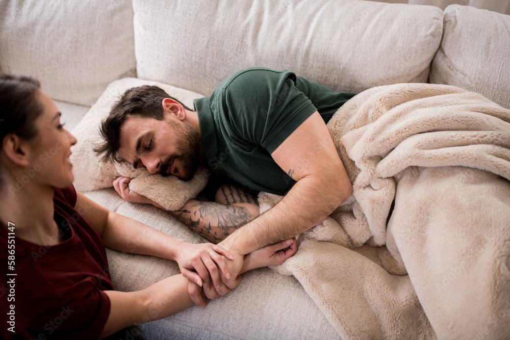 Young man taking a nap in his living room, while his wife is holding his hand. Young man taking a nap in his living room, while his wife is holding his hand.