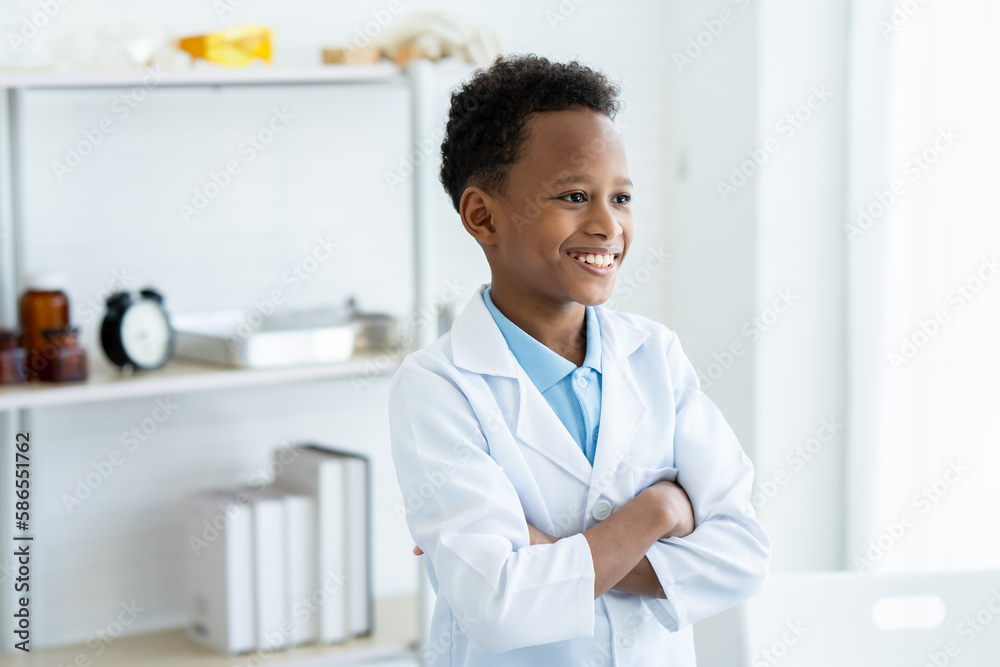 In chemistry classroom with many laboratory tools on shelves. A young African boy in white lab coat stand with arms crossed thinking and smile about new idea for next experiment while waiting teacher. In chemistry classroom with many laboratory tools on shelves. A young African boy in white lab coat stand with arms crossed thinking and smile about new idea for next experiment while waiting teacher.