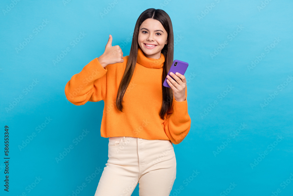 Portrait of cute positive girl hold telephone demonstrate thumb up feedback isolated on blue color background Portrait of cute positive girl hold telephone demonstrate thumb up feedback isolated on blue color background