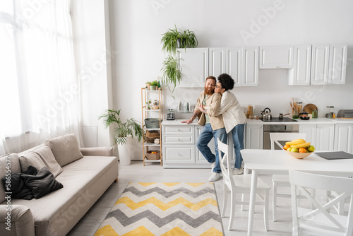 happy african american woman hugging bearded man in kitchen at home.