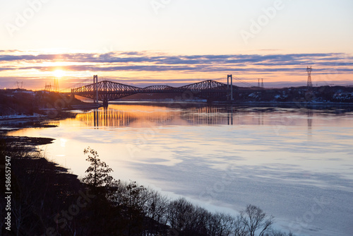 The 1970 Pierre-Laporte and the 1904 Quebec bridges over the St. Lawrence river in silhouette seen from the Cap-Rouge cliff during a beautiful pink and orange spring sunrise  Quebec City  Quebec  Cana