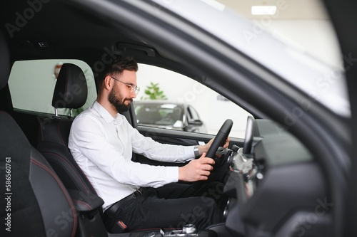 Happy caucasian man in formal wear getting inside luxury modern car for testing interior before purchase. Concept of dealership, selling and purchase