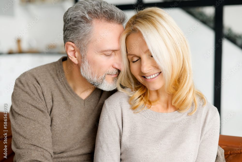 Cheerful and happy middle-aged spouses enjoying time together. Handsome grey-haired man hugging gently beautiful good-looking woman, their eyes are closed. Love and bond concept. Close-up portrait Cheerful and happy middle-aged spouses enjoying time together. Handsome grey-haired man hugging gently beautiful good-looking woman, their eyes are closed. Love and bond concept. Close-up portrait