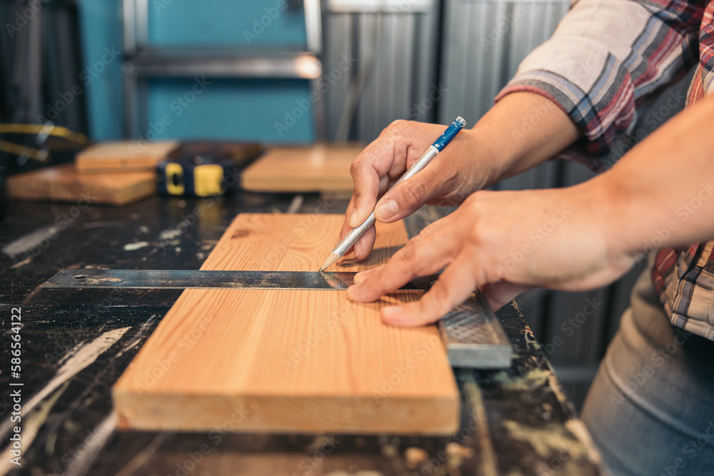 Side view of a carpenter using a pencil to draw a line on a wood