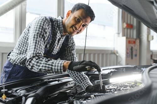 Indian car mechanic standing and working in service station. Car specialists examining the lifted car. Professional repairmen wearing mechanic uniform in blue color.